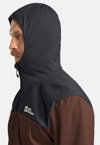 Giacca con cappuccio caratterizzata da una sezione superiore nera e una sezione inferiore marrone. Realizzata in un tessuto morbido e flessibile con chiusura a zip e dettaglio del logo.