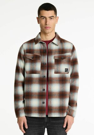 Geruite flanellen shirt in bruine, crèmekleurige en blauwe tinten. Knopsluiting aan de voorkant, twee borstzakken en een patchlogo op de linker zak. Geweven stof.
