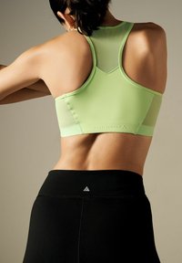 Light green athletic crop top with a racerback design, paired with high-waisted black leggings featuring a subtle logo detail.