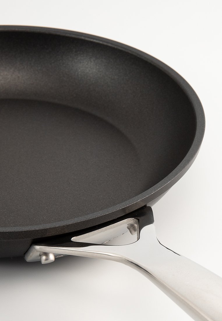 Czarna patelnia z nieprzywierającą powierzchnią, zaokrąglonymi krawędziami i stalową rączką przymocowaną z boku.