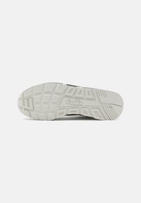 Suola delle scarpe con battistrada in gomma bianca testurizzata, caratterizzata da scanalature profonde e un dettaglio del logo. Parte superiore nera visibile nel tallone.