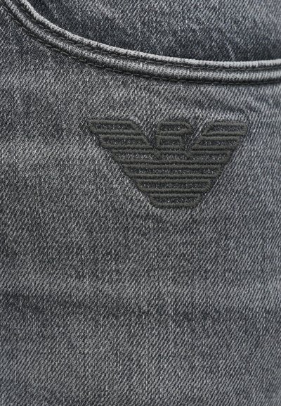 Σκούρο γκρι τζιν ύφασμα με διακριτή υφή. Διαθέτει μαύρο κομμένο λογότυπο που μοιάζει με φτερά με οριζόντιες ρίγες.
