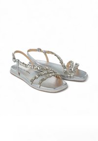 Sandalias de plata metálica con suela plana, que cuentan con adornos de strass, correas de tobillo ajustables y un diseño superior texturizado.