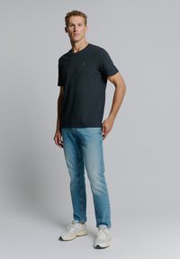 Zwarte short-sleeve t-shirt gecombineerd met lichtblauwe jeans en witte sneakers. Eenvoudig ontwerp met een lichte glans op de stof.