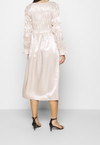 Flödande, ljusrosa satin klänning med smockad bodice och långa, rynkade ärmar som slutar strax under knäet. Buren med svarta klacksandaler.