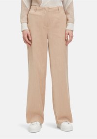 Beige corduroy wijd-uitlopende broeken met gestructureerde verticale strepen, met een aansluitende taille en zijzakken. Accessoires zijn witte sneakers.