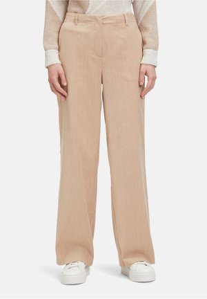 Beige kordfløjl brede bukser med teksturerede lodrette striber, der har en tætsiddende talje og sidelommer. Tilbehøret inkluderer hvide sneakers.