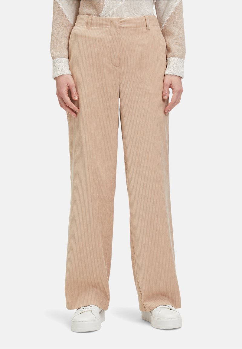 Beige corduroy wijd-uitlopende broeken met gestructureerde verticale strepen, met een aansluitende taille en zijzakken. Accessoires zijn witte sneakers.