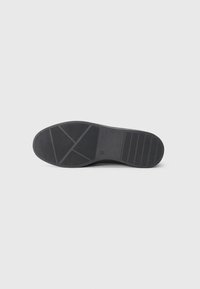 Suela de zapato de goma negra con patrones de agarre texturizados y relieves; incluye líneas horizontales y diagonales para tracción.