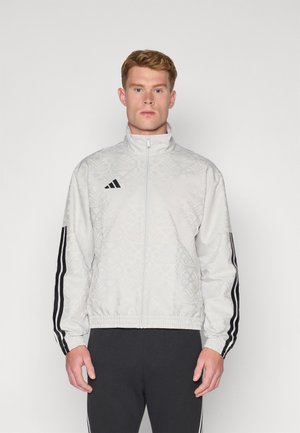 Lys grå bomberjakke med et subtilt præget mønster, sort Adidas-logo og sorte stribede detaljer på ærmerne, afsluttet med elastisk kant.