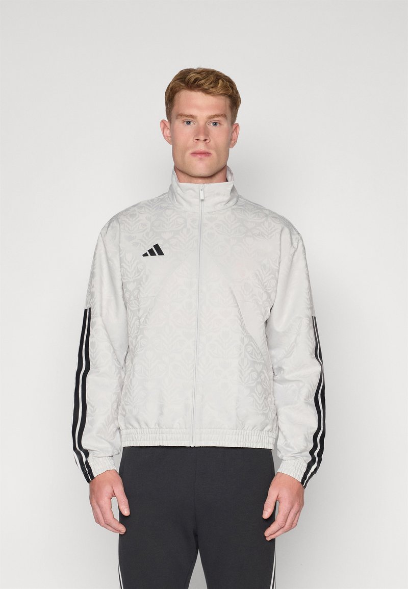 Casaco bomber cinza claro com um padrão em relevo subtil, logótipo preto da Adidas e detalhes em preto nas mangas, finalizado com uma bainha elástica.