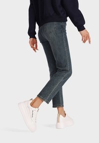 Jeans in denim blu con taglio dritto, dotati di tasche posteriori e un lavaggio sbiadito. Abbinati a sneakers bianche, che mettono in risalto un design pulito.