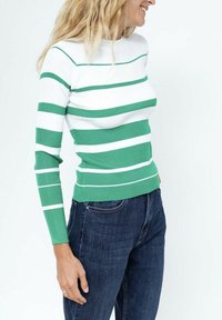 Pull à rayures vertes et blanches, en côtes, avec un col haut, une coupe ajustée et des manches longues, accompagné d'un jean bleu foncé.