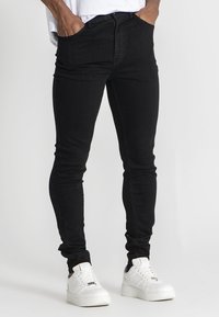 Mustat slim-fit farkut hienolla kangasrakenteella, joissa on etutaskut ja vetoketju. Yhdistetty valkoisiin tennareihin kontrastiksi.