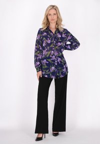 Camicia a maniche lunghe con bottoni in blu navy con stampa floreale viola. Abbinata a pantaloni neri a gamba larga e tacchi alti neri.