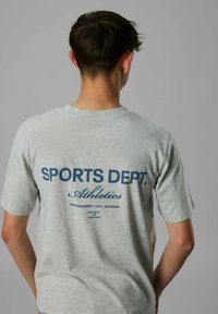 Grå bomulds t-shirt med "SPORTS DEPT. Athletics" i marineblå på bagsiden, med rund hals og korte ærmer.
