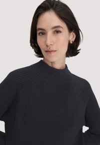 Schwarzer, strukturierter Pullover mit hohem Kragen und Rippmuster, der Raglanärmel und eine enge Passform bietet. Schlichtes Design, ohne Verzierungen.