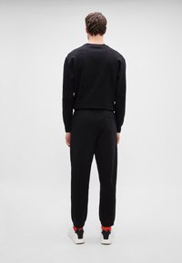 Juodas sportinis kostiumas, pagamintas iš medvilnės, laisvas kirpimas, banguotos rankovės, jogerio kelnėse yra užpakalinis kišenė, derinamas su baltais sportbačiais ir raudonomis kojinėmis.