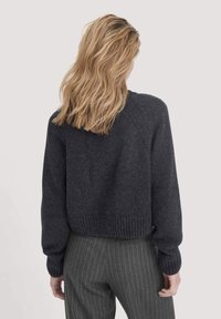 Dunkelgrauer, gestrickter Pullover mit einem cropped Design, Raglanärmeln und gerippten Bündchen und Saum. Weiche Textur, kombiniert mit gestreiften Hosen.