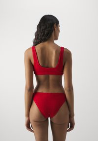 Rød strikket bikiniset med en scoop-back topp og høy midje-bunn. Teksturen er ribbet med en sømløs design.