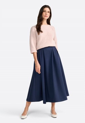 Maglione rosa chiaro con texture e maniche a ¾ abbinato a una gonna midi plissettata blu navy. Le scarpe con tacco bianche completano l'outfit.