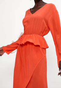 Oranges Kleid mit V-Ausschnitt, langen Ärmeln und einer Peplum-Taille. Verfügt über einen Bindegürtel und einen asymmetrischen Saum. Aus glattem, leichtem Stoff.