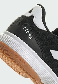 Chaussure de sport noire avec tige en textile, accents blancs et semelle en caoutchouc. Présente la marque "LIGRA" et des détails texturés au niveau du talon.