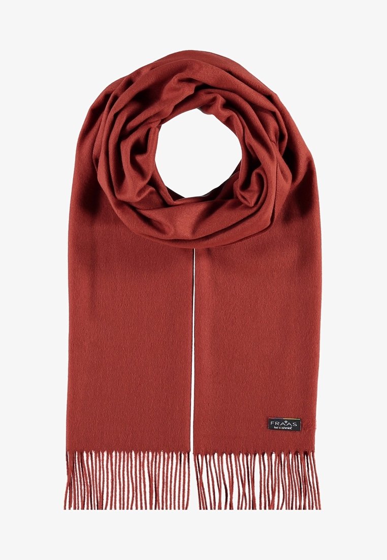 Écharpe en laine douce couleur rouille avec des franges aux extrémités et une petite étiquette noire cousue près d’un bord.