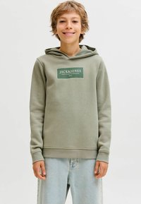 Žalias džemperis su kapišonu, su baltu logotipo pleistru ant krūtinės. Pagamintas iš minkštos medžiagos, su raštuotais rankogaliais ir apatine dalimi. Dėvimas su šviesiai mėlynomis džinsomis.