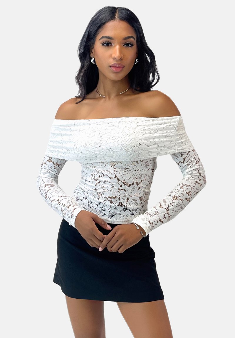 Top blanco de encaje sin mangas con mangas largas sobre una falda negra. El encaje presenta patrones florales y un diseño ajustado.