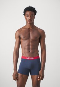 Mörkblå kalsonger med röd elastisk midjeband som har "Levi's"-logotypen. Mjuk tyg, figursydd design, slät textur och längd till mitten av låret.