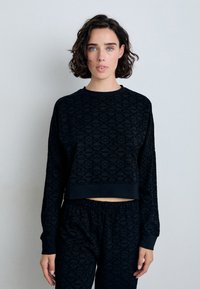 Svart cropped sweatshirt med lange ermer, preget geometrisk mønster, rund hals, og ribbede mansjetter, kombinert med matchende svarte bukser.