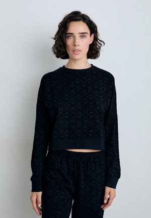 Svart cropped sweatshirt med lange ermer, preget geometrisk mønster, rund hals, og ribbede mansjetter, kombinert med matchende svarte bukser.