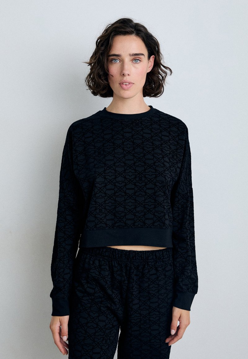 Svart cropped sweatshirt med lange ermer, preget geometrisk mønster, rund hals, og ribbede mansjetter, kombinert med matchende svarte bukser.