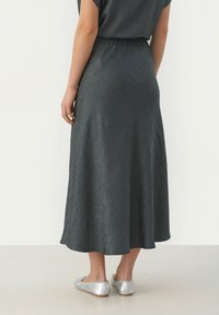 Lange, donkergrijze rok van gekreukt materiaal, met een elastische tailleband en een vloeiende design, gecombineerd met zilveren platte schoenen.