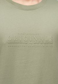 Ανοιχτοπράσινο μπλουζάκι με ανάγλυφα γράμματα «Nineteen Ninety Originals 1990 Brought to you by Jack & Jones» στο στήθος.