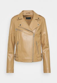 Veste de biker en cuir tan avec col cranté, fermeture éclair asymétrique et boucles décoratives sur les côtés. Texture lisse avec des accents en métal argenté.