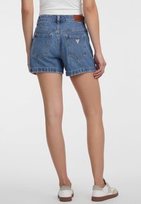Shorts in denim con un colore blu sbiadito, orlo sfrangiato, due tasche posteriori e una patch in cuoio sulla cintura. Design casual.