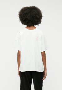 Valge lühikeste varrukatega T-särk ümmarguse kaelusega, mille tagaküljel õlavarre lähedal on väike roosa "Puhkeklubi" logo. Pehme puuvillane materjal.