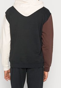 Mikina s kapucí v barevných blocích obsahující černé, krémové a vínové části. Vyrobena z měkké bavlny, s kapucí a žebrovanými manžetami. Minimální značení.