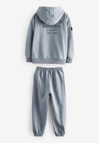 Grå bomulds hoodie med en lomme foran og elastiske manchetter, parret med matchende joggingbukser med elastisk talje.