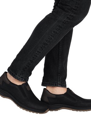 Black slip-on shoes with brown accents, featuring a smooth leather upper, elastic side panels, and a rubber outsole for traction.