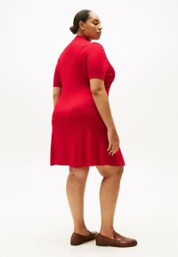 Rotes geripptes Strickkleid mit kurzen Ärmeln, ausgestelltem Saum und Rundhalsausschnitt, kombiniert mit braunen Slippern. Glatte Textur und figurbetontes Design.