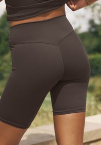 Magas derekú, sötétbarna kerékpáros rövidnadrágok, rugalmas anyagból, lapos varrással és combközépig érő szabással a kényelem és a mozgásszabadság érdekében.