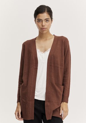 Brown loose-fit cardigan made from soft knit with a V-neck, two front pockets, and ribbed cuffs, layered over a white lace-trimmed top.