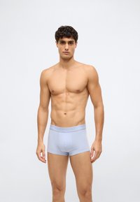 Světle modré bavlněné boxerky s měkkým páskem, na kterém je logo Calvin Klein, prezentované na modelu na neutrálním pozadí.