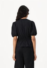 Svart topp med puffärmar, elastisk midja och rynkad design. Slät tyg med en enhetlig färg; inga ytterligare mönster eller detaljer.