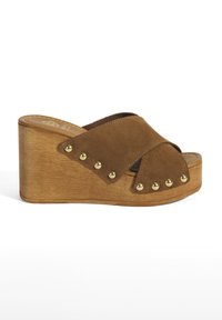 Sandales à talons en cuir suédé marron avec des bretelles entrecroisées, talon en bois et clous dorés le long des bords. Semelle plate pour le soutien.