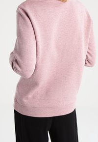 Rosa sweatshirt med en texturerad yta, rund halsringning och långa ärmar. Nederkanten är något ribbad, i kombination med svarta byxor.