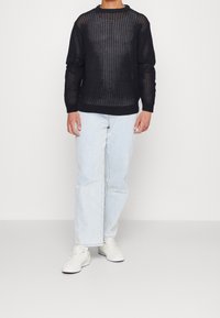 Pull noir en maille avec un motif en maille, col rond, poignets côtelés, assorti à un jean droit bleu clair et des baskets blanches.